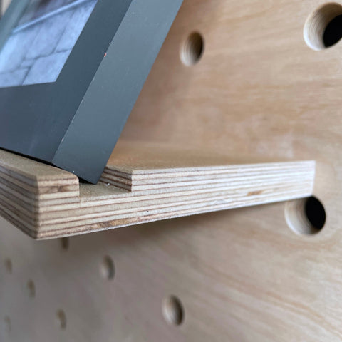 detail of wooden shelf with groove for pegboard with picture frame to prevent sliding off