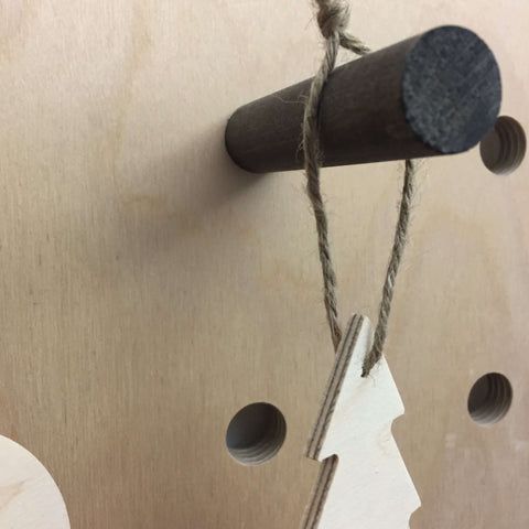 wooden tree decoration hanging from a peg hook with string at pegboard