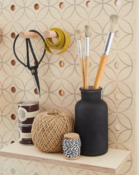 wooden shelf with string, paint pots and scissor hanging on wooden peg on large pegboard printed with graphic florals