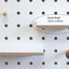 Small wood shelf in white plywood shown on white pegboard. Shelf is fitted with pegs to slot into pegboard. Made by Kreisdesign in UK