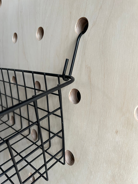 detail of hooks and wire basket hanging off wooden pegboard by kreisdesign