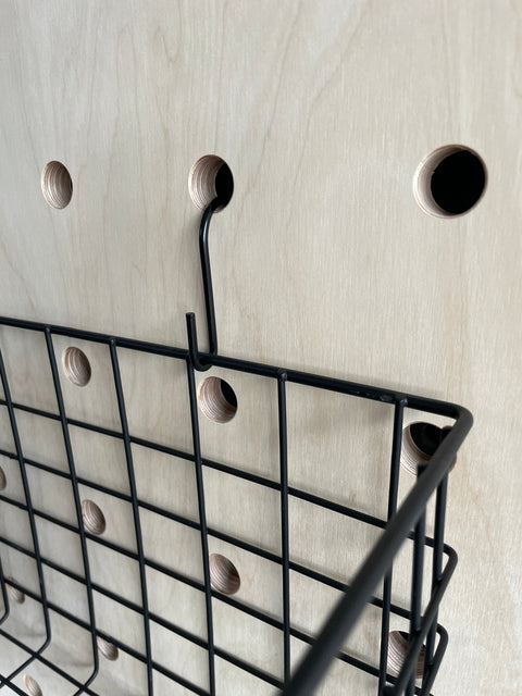 detail of black metal hook thread through hole of pegboard where the black metal wire basket is hanging off