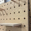 Wooden pegboard with holes and hooks on a light background