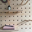 detail of shelves and pegs with accessories of a maple veneer plywood pegboard by kreisdesign. books and a round picture frame hanging off a beech peg