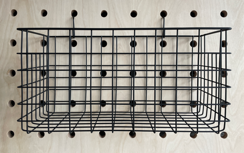 black wire basket hanging from hooks off pegboard by kreisdesign