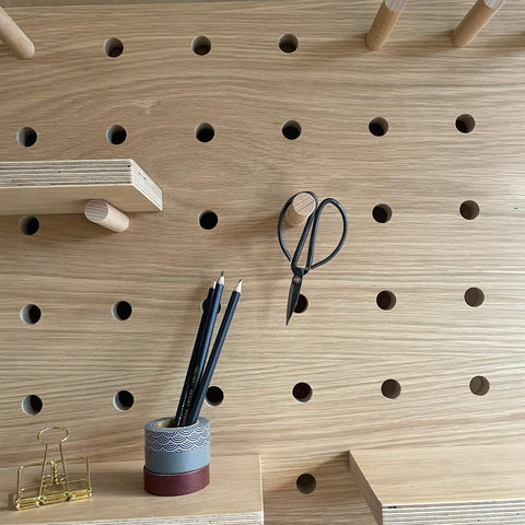 oak peg board with desk accessories placed on shelves and hung from peg hoook